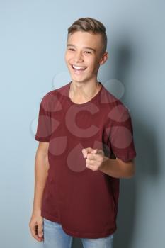 Smiling teenage boy pointing at viewer on color background�