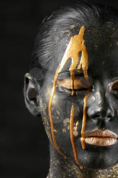 Beautiful woman with black and golden paint on her body against dark background, closeup�