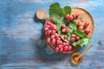 Ripe grapes and bowl with honey on wooden table�