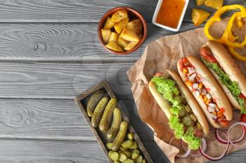 Tasty hot dogs with vegetables and sauce on wooden table�
