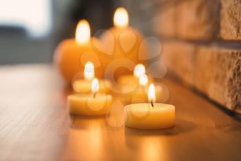 Beautiful burning candles on wooden table near brick wall�