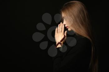 Beautiful young woman praying on dark background�