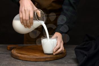 Woman pouring fresh milk from jug into glass on table�