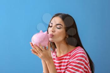Beautiful young woman with piggy bank on color background�