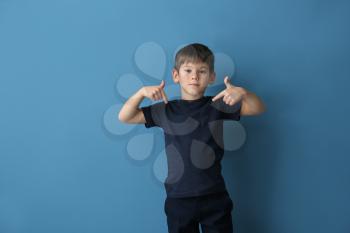 Cute little boy pointing at his t-shirt on color background�