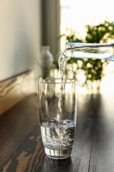 Pouring of fresh water from bottle into glass on wooden table�