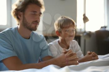 Father with son praying near bed at home�