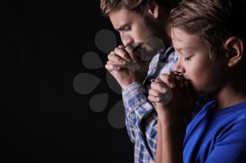 Praying father and son on dark background�