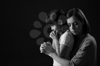 Praying mother and daughter on dark background�