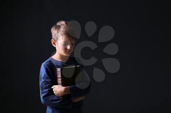 Portrait of praying boy with Bible on dark background�