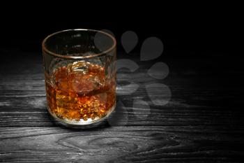 Glass of whisky with ice on wooden table against black background�