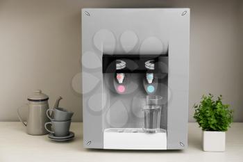 Modern water cooler with glass on kitchen table�