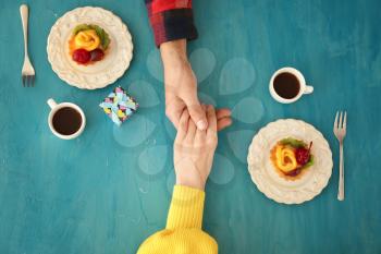 Loving young couple with coffee and desserts on color table�