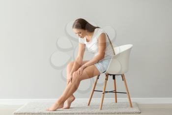 Woman suffering from pain in leg while sitting on chair near light wall�