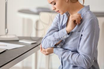 Young woman suffering from pain in elbow at workplace�