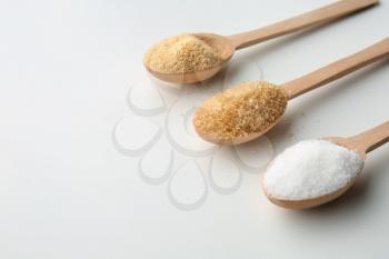 Different granulated sugar in wooden spoons on white background�