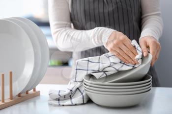 Woman wiping plate with towel in kitchen�