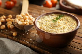 Bowl with tasty hummus on wooden board, closeup�