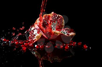 Tasty fresh pomegranate and splashing juice on black background�