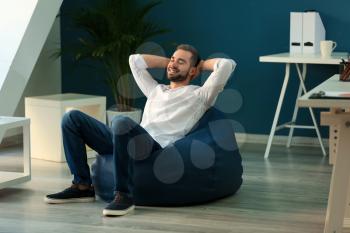 Young businessman sitting on beanbag chair in office�