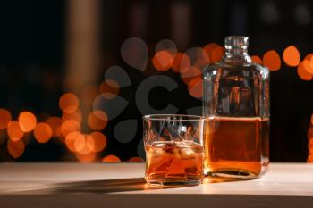 Glass and bottle of whiskey on wooden table against blurred lights�
