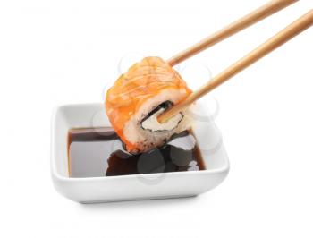 Dipping of tasty sushi roll into bowl with sauce on white background�
