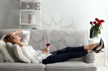 Tired woman with glass of wine on sofa at home�