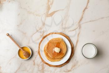 Hot tasty pancakes with glass of milk and honey on light table�