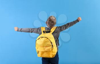 Happy little schoolboy with backpack on color background�