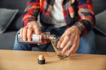 Man pouring alcohol from bottle into glass at table, closeup. Alcoholism concept�