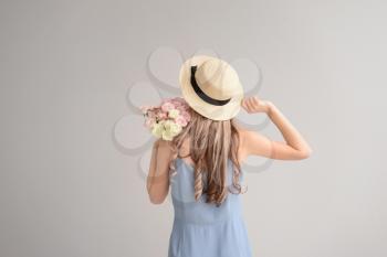Beautiful young woman with bouquet of flowers on grey background, back view�