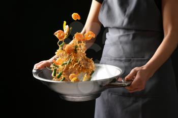 Woman cooking tasty Chinese noodles in wok on dark background�