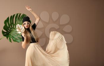 Beautiful woman with tropical leaves on color background�