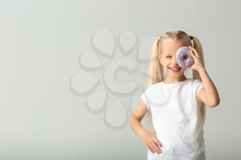 Cute little girl with donut on light background�