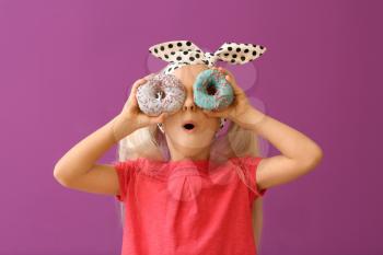 Cute little girl with donuts on color background�