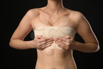 Woman with bandage on her chest against dark background. Breast augmentation concept�
