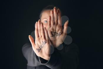 Text STOP SUICIDE written on palms of woman against dark background�