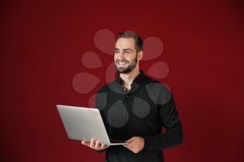 Young businessman with laptop on color background�