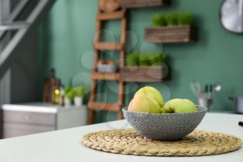 Wicker bowl with fresh apples on light table in kitchen�