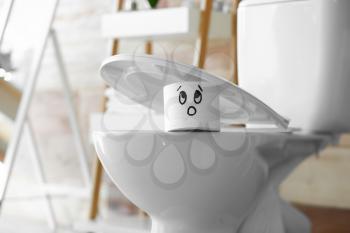 Roll of paper with funny drawn face under seat of toilet bowl�
