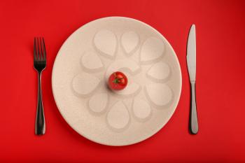 Plate with one tomato and cutlery on color background. Diet concept�
