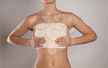 Woman with bandage on her chest against grey background. Breast augmentation concept�