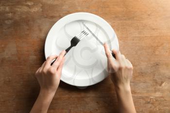 Female hands with cutlery and empty plate on wooden background�