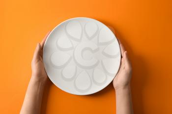 Female hands with empty plate on color background�
