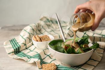 Pouring of tasty tahini from jar onto fresh vegetables in bowl�