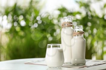 Glass and bottles of fresh milk on table outdoors�