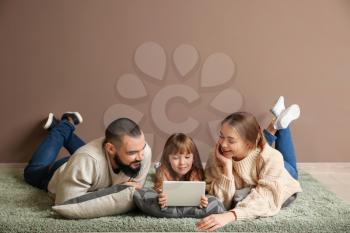 Happy family with tablet computer lying on carpet near color wall�