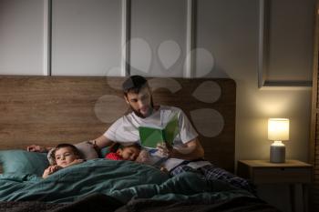 Young father reading book for his children in bed�