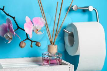 Roll of toilet paper hanging on color wall with reed diffuser in restroom�