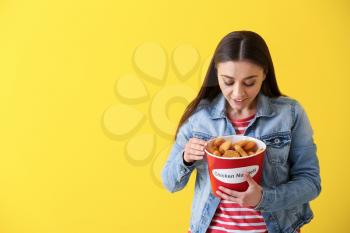 Beautiful woman with bucket of tasty nuggets on color background�